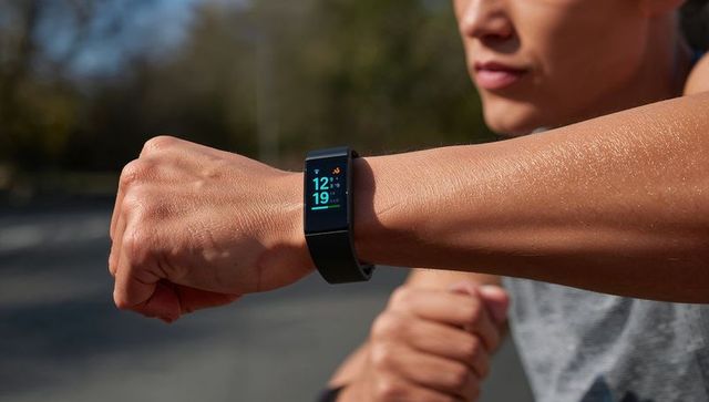 Male runner checking fitness tracker on wrist during outdoor run, sunlit closeup, bright screen
