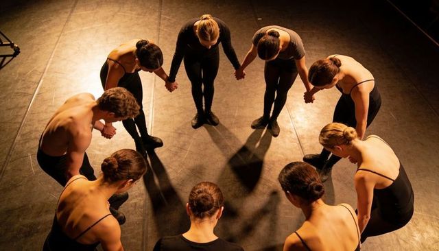Contemporary dancers bowing in hand-holding circle under warm stage spotlights, unity