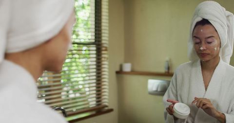 Biracial Woman Applying Skincare Product in Bathroom Reflection