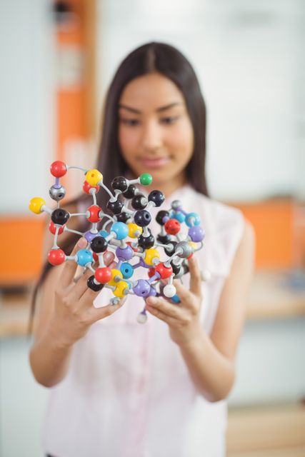 Attentive schoolgirl experimenting molecule model in laboratory at school