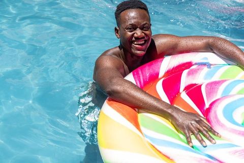 Smiling african man enjoying sunny pool with vibrant rainbow swirl inflatable