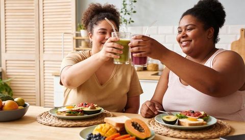 Friends toasting vibrant smoothies over avocado toast breakfast at cozy kitchen table