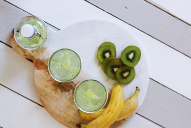 Green smoothie with kiwi and banana displayed on a white wood background. Ideal for healthy living promotions, summer drink recipes, and refreshing beverage advertisements.