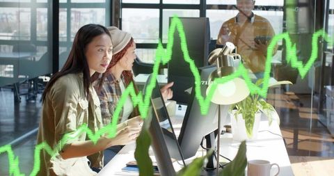 Young professionals analyzing financial charts on desktop computers in modern coworking office