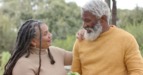 Senior couple sharing tender moment in garden holding green apples wearing knit sweaters