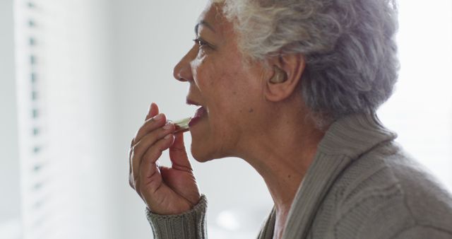 Senior woman taking medication in a well-lit room. Useful for healthcare, elderly care, self-care, and medical advertisements, showcasing private care routines.