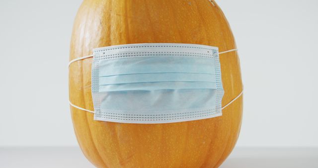 A pumpkin with a surgical mask covering its face reflects pandemic-related safety measures during Halloween. Perfect for content on health and safety tips, humorous takes on traditional holidays, or themed social media posts highlighting the intersection of festivity and current events.