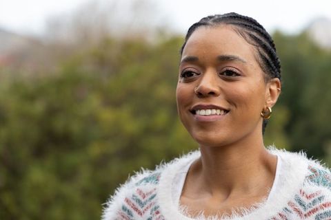 African american woman smiling outdoors wearing fuzzy sweater, braided hair, hoop earrings