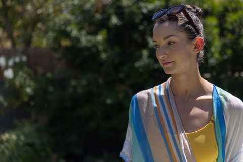 Woman standing looking right wearing yellow swimsuit and striped coverup in sunlit garden