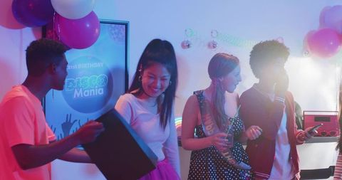 Diverse friends celebrating disco birthday party holding gifts dancing under neon balloons