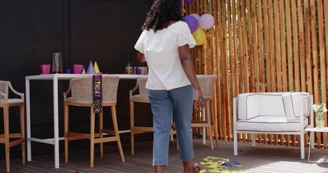 African American woman walking toward balloons on deck celebrating backyard birthday party