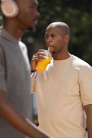 African american man sipping orange juice during sunny urban stroll