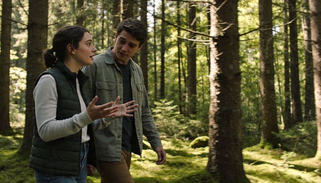 Young couple walking and talking through sunlit mossy forest, candid conversation on trail