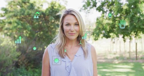 Standing woman wearing striped blouse presenting sustainable data overlay in sunlit orchard