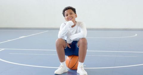 Youthful Athlete Balancing on Basketball in Gym Court