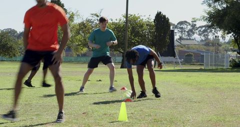 Diverse athletes performing cone agility drill on sunny park field for fitness training