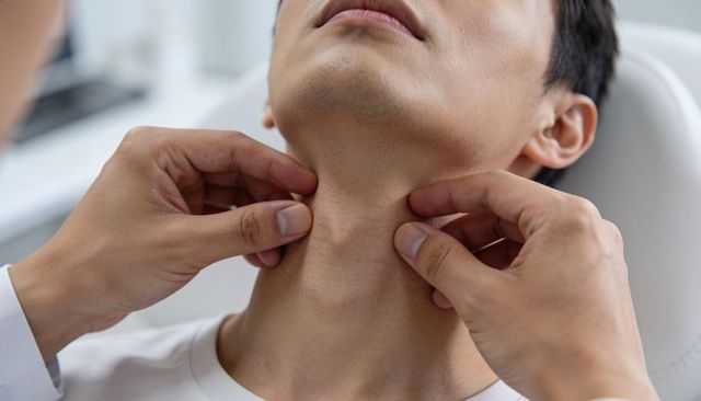 Doctor palpating neck of asian man during clinical throat exam