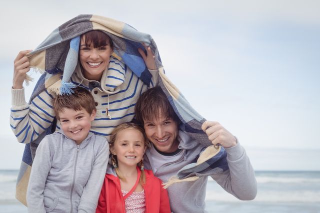 Family enjoying a winter day at the beach, smiling and bonding under a blanket. Perfect for use in advertisements, family-oriented content, travel promotions, and lifestyle blogs.