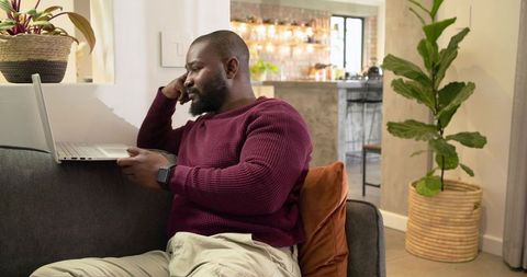 African American man working from home on laptop in cozy modern living room with plants