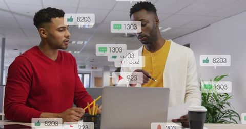 Collaborating over social media analytics on laptop in modern open office, pointing at screen
