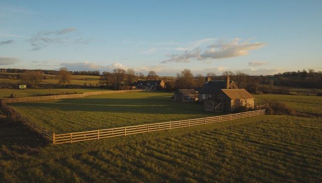 Idyllic Countryside Farm at Sunset with Fenced Paddock and Barns