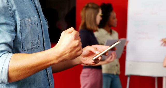 Excited Businessman Using Smartphone with Colleagues in Background - Download Free Stock Images Pikwizard.com