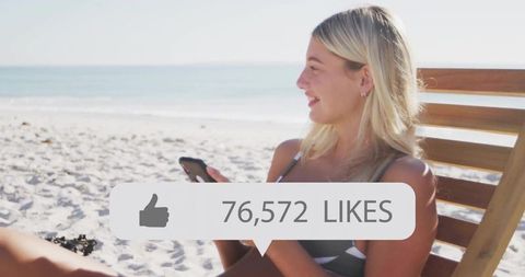 Blonde woman on slatted beach chair using smartphone with 76,572 likes overlay, sunlit beach