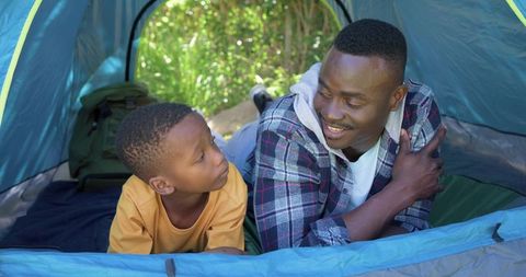 African american father and son sharing conversation inside blue tent during camping trip