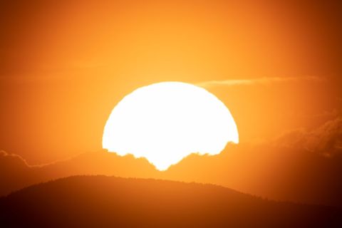 Sun rising behind mountain silhouette during golden sunrise with vivid orange sky