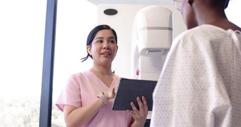 Female Radiology Technologist Holding Tablet Explaining Mammogram Positioning to Patient
