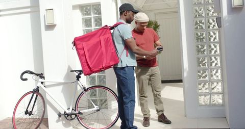 African american bicycle courier delivering takeout while recipient checking smartphone
