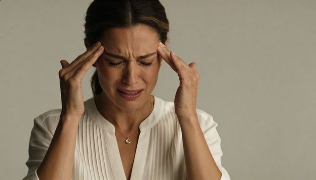 Woman pressing temples, showing migraine pain and stress, white blouse studio portrait