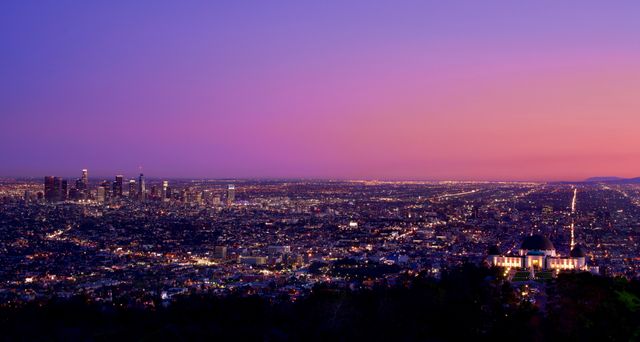 Los Angeles skyline at dusk with a view of Griffith Observatory illuminated against the evening sky. Ideal for use in travel blogs, brochures, and websites, this scenic cityscape highlights urban beauty and iconic landmarks amid a stunning sunset backdrop. Perfect for cultural or city-themed projects.