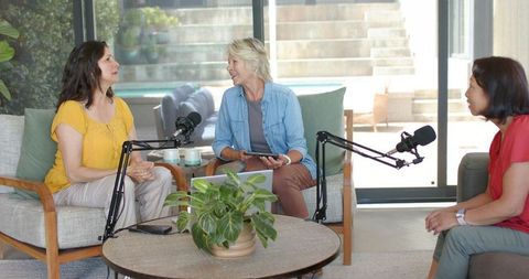 Diverse women recording podcast in cozy living room around coffee table discussion