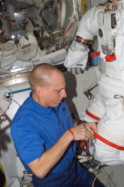Astronaut working with spacesuit in International Space Station airlock, ideal for topics on space travel, astronaut activities, space station life, or NASA missions.