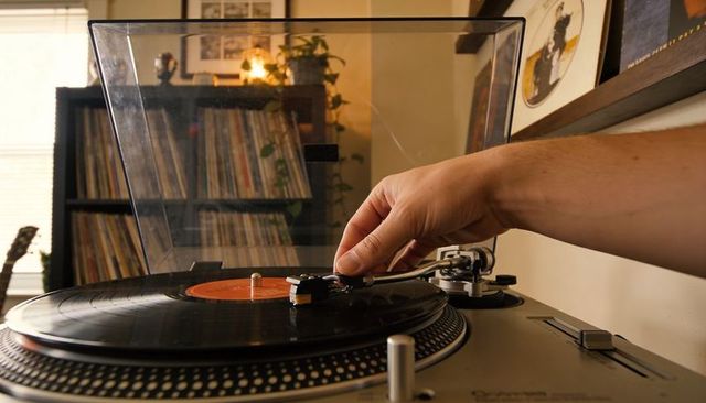 Right hand adjusting tonearm on vintage turntable with vinyl collection and warm lighting