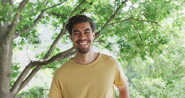 Portrait of cheerful biracial man in yellow t-shirt is standing against trees. happiness and domestic lifestyle.