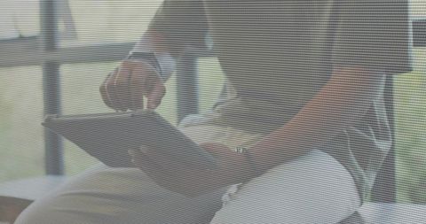 Man tapping tablet on bench by paned window wearing olive shirt and wristwatch in daylight