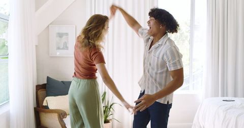 Diverse Couple Joyfully Dancing in Bright, Cozy Bedroom
