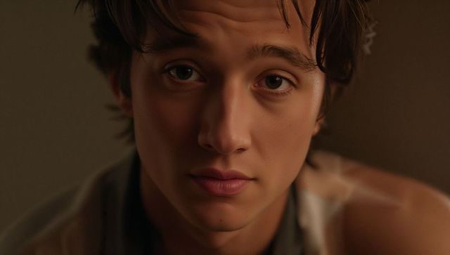 Pensive young man headshot with tousled hair, warm soft lighting, intimate closeup gaze