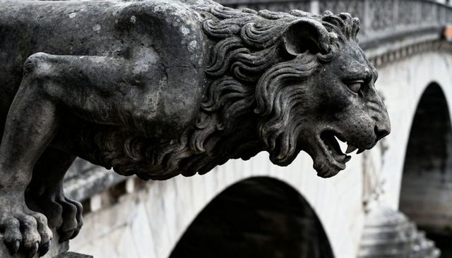Weathered stone lion gargoyle roaring from historic bridge, lichen-covered arches detail