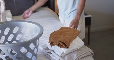 Man folding towels and organizing laundry basket on bed for home linen care and tidy bedroom