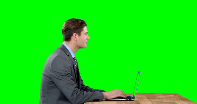 Businessman typing on laptop at desk with green screen background. Ideal for corporate presentations, remote work scenes, technology advertisements, and office-related videos or content. Green screen area allows for easy background customization.