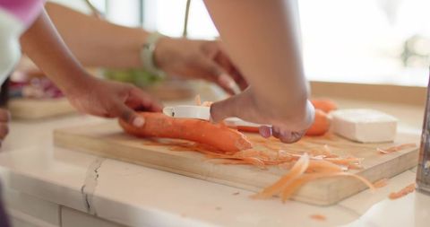 African american mother and child peeling carrot together on bright kitchen countertop