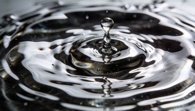 Crystal water droplet rising on dark surface creating concentric ripples and glossy highlights