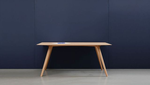 Minimalist oak table featuring splayed legs and navy backdrop with notebook and pen
