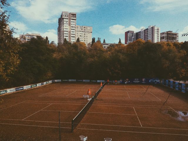 Shows an empty cement tennis court surrounded by autumn trees and city buildings in the background under a clouded sky. Perfect for illustrating urban recreational sports, promoting outdoor activities, or highlighting sports facilities in residential areas.