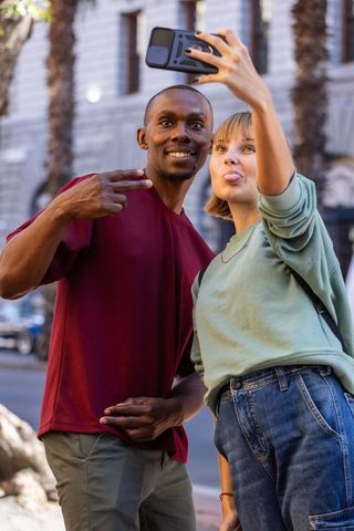 Diverse friends taking playful selfie on urban sidewalk holding smartphone with camera bump