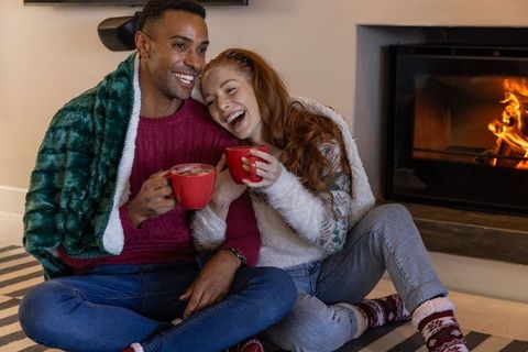 Happy Couple Relaxing by Fireplace with Hot Drinks in Cozy Atmosphere