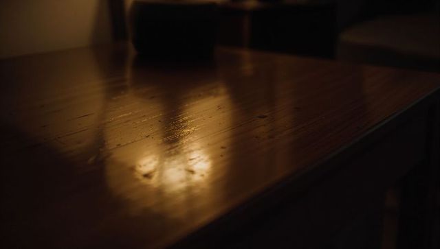 Varnished wood tabletop reflecting warm light, soft bowl bokeh, rich grain and patina
